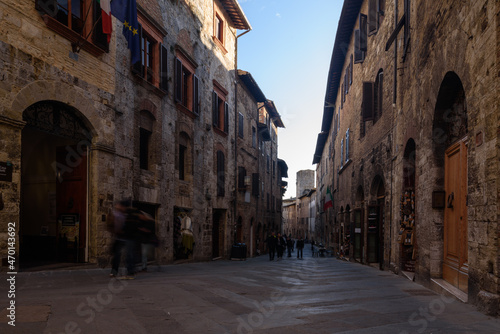Gasse in San Gimignano i schatten mit Fassaden und Personen bei blauem Himmel