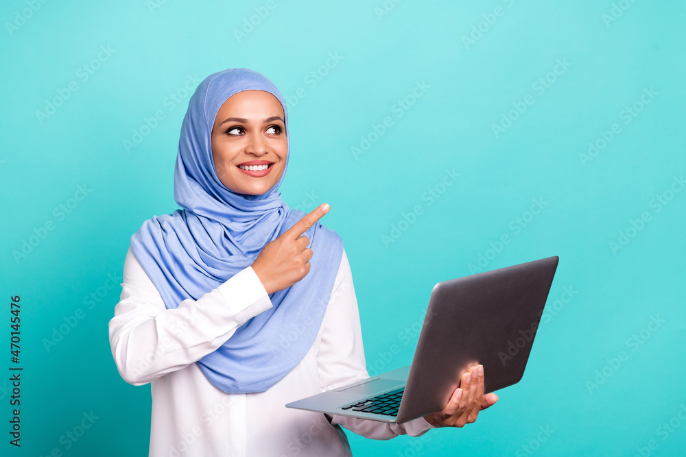 Photo of adorable sweet young lady dressed islamic hijab smiling pointing empty space modern device isolated teal color background