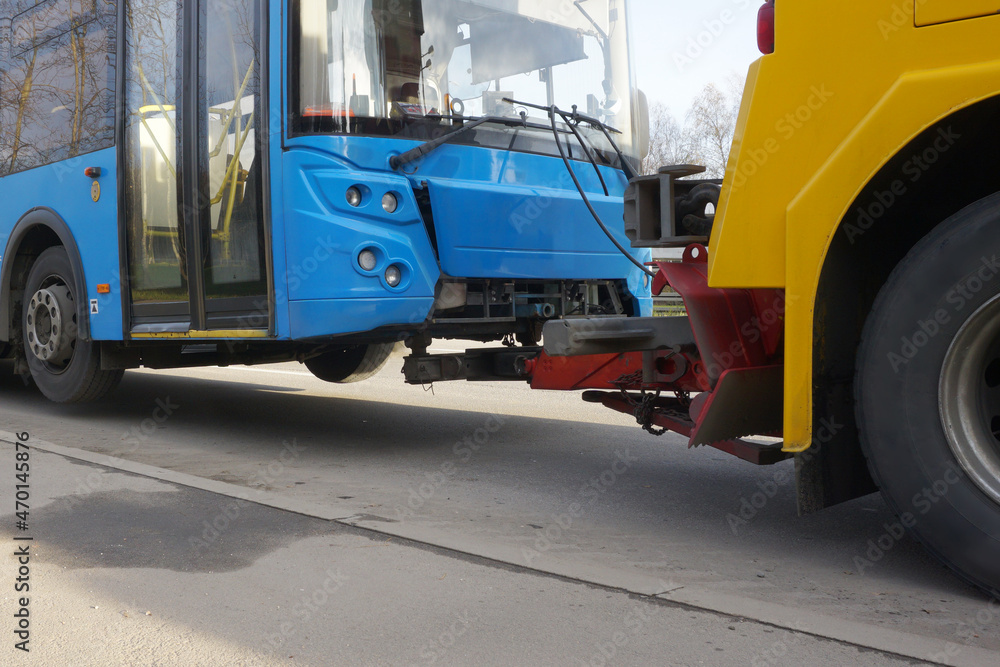 Fototapeta premium A tractor is towing a faulty bus along a city street. Bus towing with partial loading.