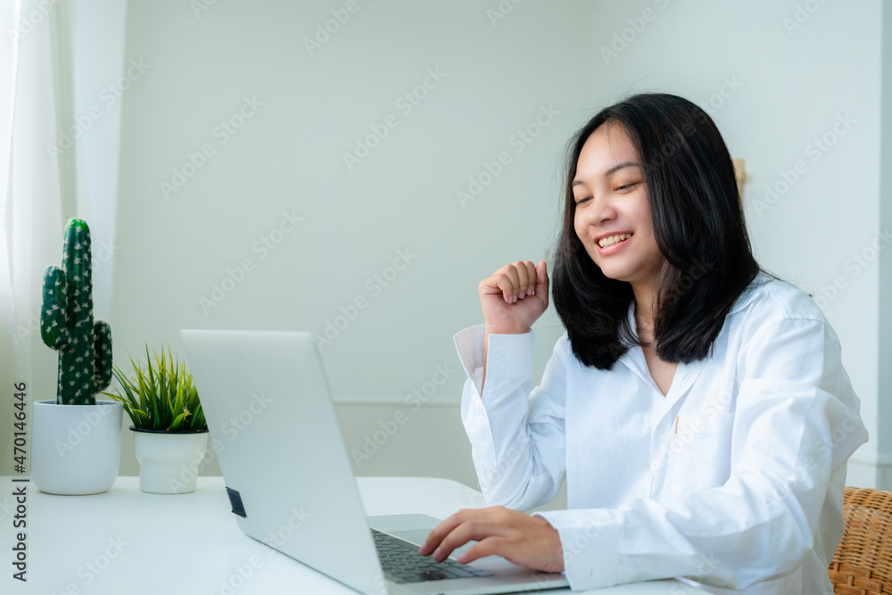 Portrait Cute Asian teen with long hair Wearing a white shirt, sitting online studying with a laptop computer on the bedroom table looks very happy. Portrait Cute Asian teen with long hair Wearing a white shirt, sitting online studying with a laptop computer on the bedroom table looks very happy.
