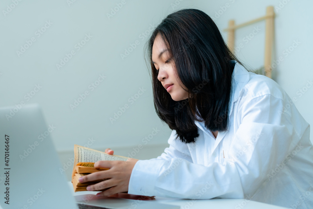 Portrait Cute Asian teen with long hair wearing a white shirt and reading a book and study online with a laptop computer on the table Portrait Cute Asian teen with long hair wearing a white shirt and reading a book and study online with a laptop computer on the table