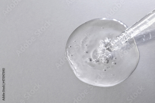 Facial serum with bubbles pouring from glass pipette on grey background. Anti aging liquid gel macro. Cosmetic product for skin care. Beauty routine. Copy space, top view, flat lay