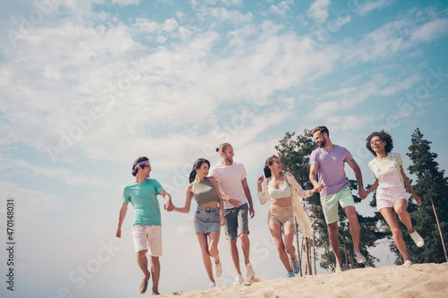 Photo of cute funky young six friends wear casual clothes smiling holding arms walking running fast outside countryside