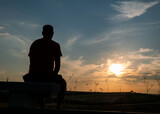 A back view of a human silhouette of a man sitting at sunset on a stone bench in a field