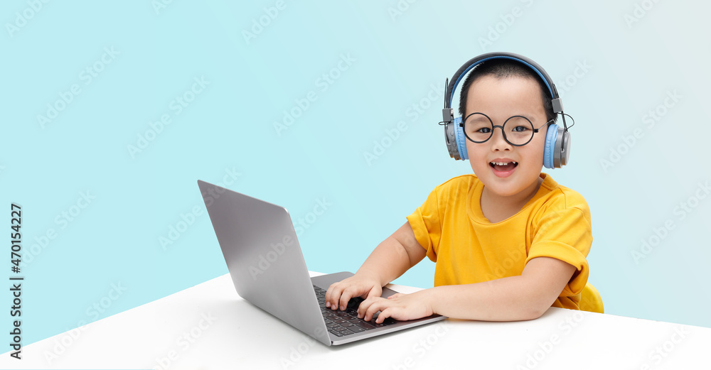 A little boy wearing headphones and using a laptop is delighted to be learning online. A little boy wearing headphones and using a laptop is delighted to be learning online.