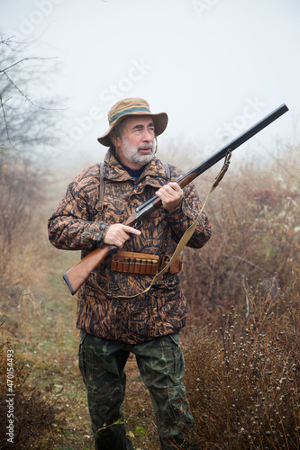 hunter man with a gray beard in hunter suit makes aiming wiring with a double-barreled rifle 