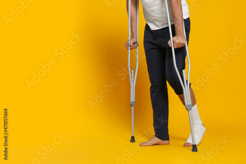 Foto Man with injured leg using crutches on yellow background, closeup