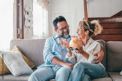 Happy caucasian couple holding piggy bank to save money to make their future dreams come true. Loving man and woman holding piggy bank for savings and discussing while sitting on sofa at home