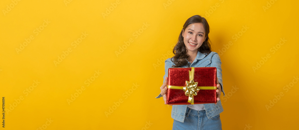 New Year. asian female in denim Jacket clothing smiling with red gift box board with copy space area for text on yellow background, holiday festival, christmas celebration, happy valentine day concept