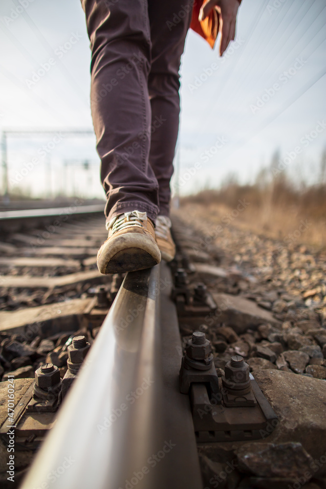 Male feet in yellow boots walk confidently along the railroad tracks, against a blurred background. Dangerous walk. Male feet in yellow boots walk confidently along the railroad tracks, against a blurred background. Dangerous walk.