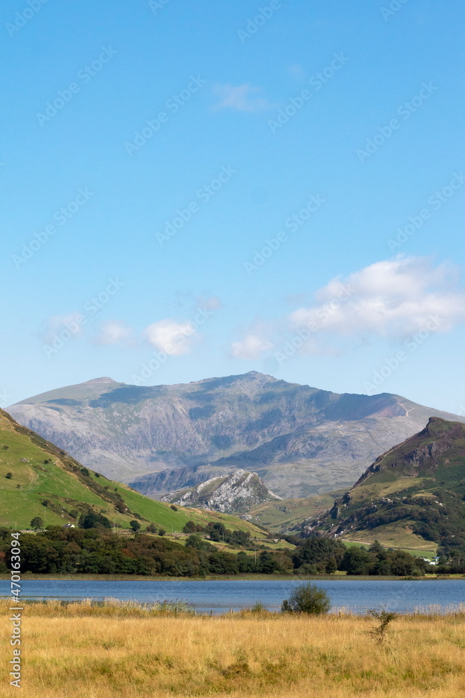 Beautiful lake Nantlle, Snowdonia, Wales. Vertical shot with foreground of water and meadow. Dramatic, rugged Mount Snowdon in the background. Copy space.