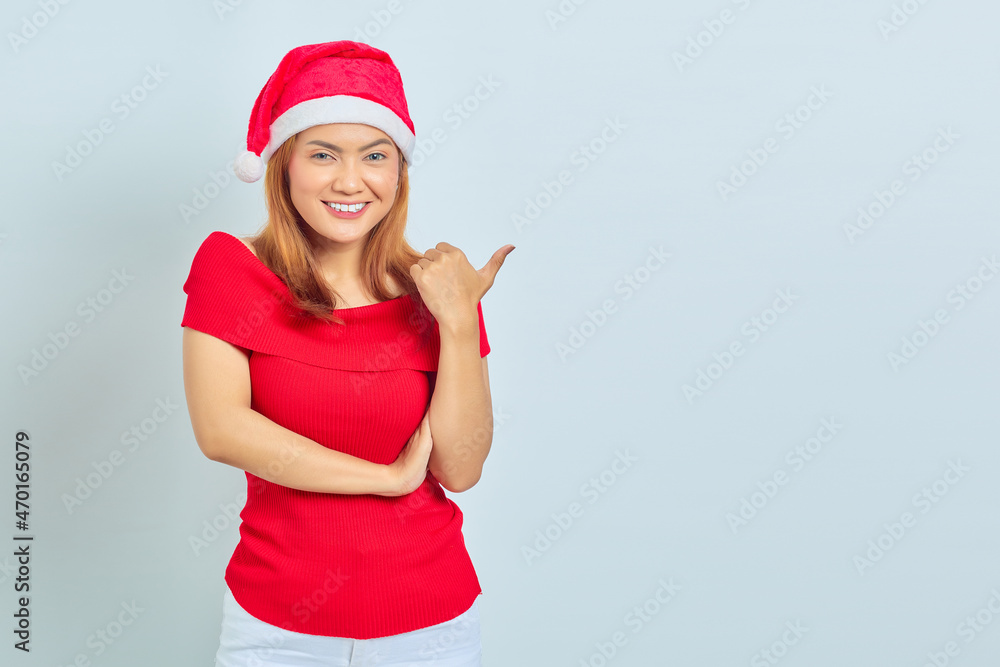 Photo of beautiful Asian girl in christmas hat with smiling facial expression and pointing aside on white background Photo of beautiful Asian girl in christmas hat with smiling facial expression and pointing aside on white background