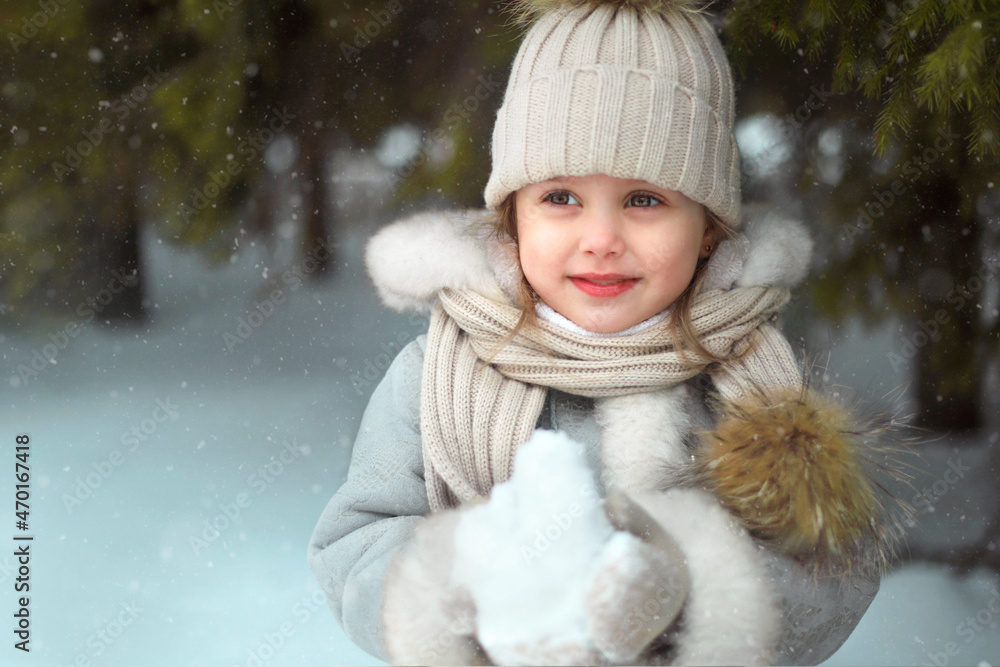 Little beautiful girl in a hat in the winter forest stands in the snow and catches snowflakes. Little girl having fun on winter day. Close-up portrait. Christmas holiday. Little beautiful girl in a hat in the winter forest stands in the snow and catches snowflakes. Little girl having fun on winter day. Close-up portrait. Christmas holiday.