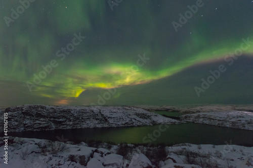 Rocks and a lake in winter, the northern lights in the sky. © Moroshka