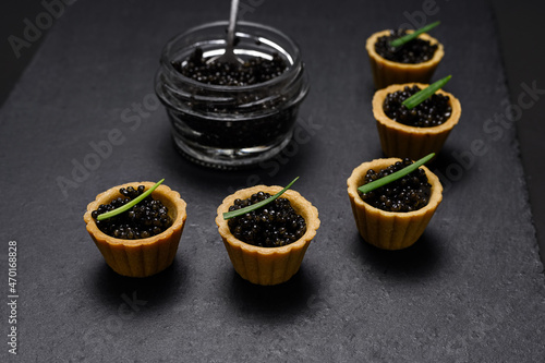 a traditional Russian dish - tartlets with black beluga caviar  decorated with green onion feathers