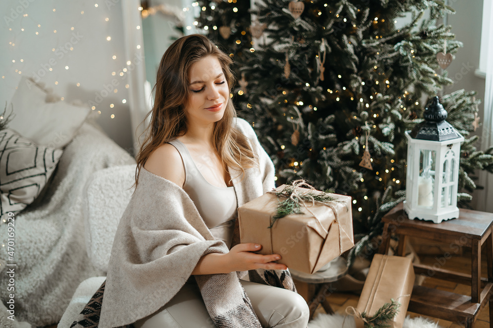Smiling sincere beautiful young woman in comfortable light winter clothes holds out a wrapped gift box to the camera, prepares a Christmas present, celebrates the winter holidays Smiling sincere beautiful young woman in comfortable light winter clothes holds out a wrapped gift box to the camera, prepares a Christmas present, celebrates the winter holidays