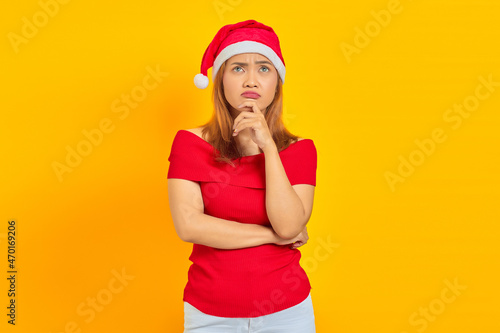 Pensive young woman wearing Christmas hat thinking about something on yellow background © Bangun Stock Photo