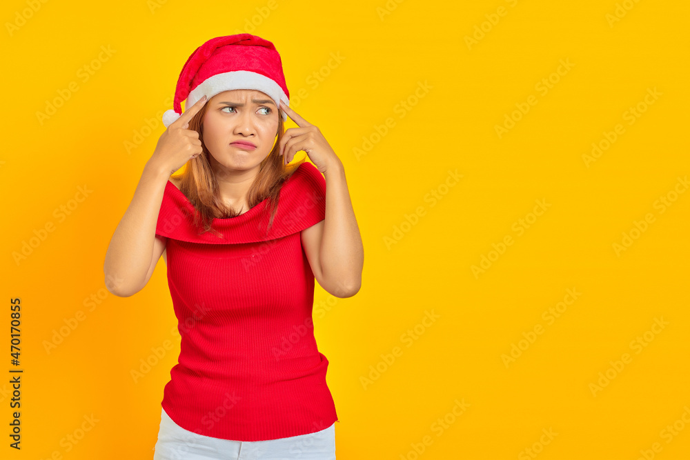 Portrait of a pensive young woman wearing Christmas hat having doubts and thinking on yellow background Portrait of a pensive young woman wearing Christmas hat having doubts and thinking on yellow background