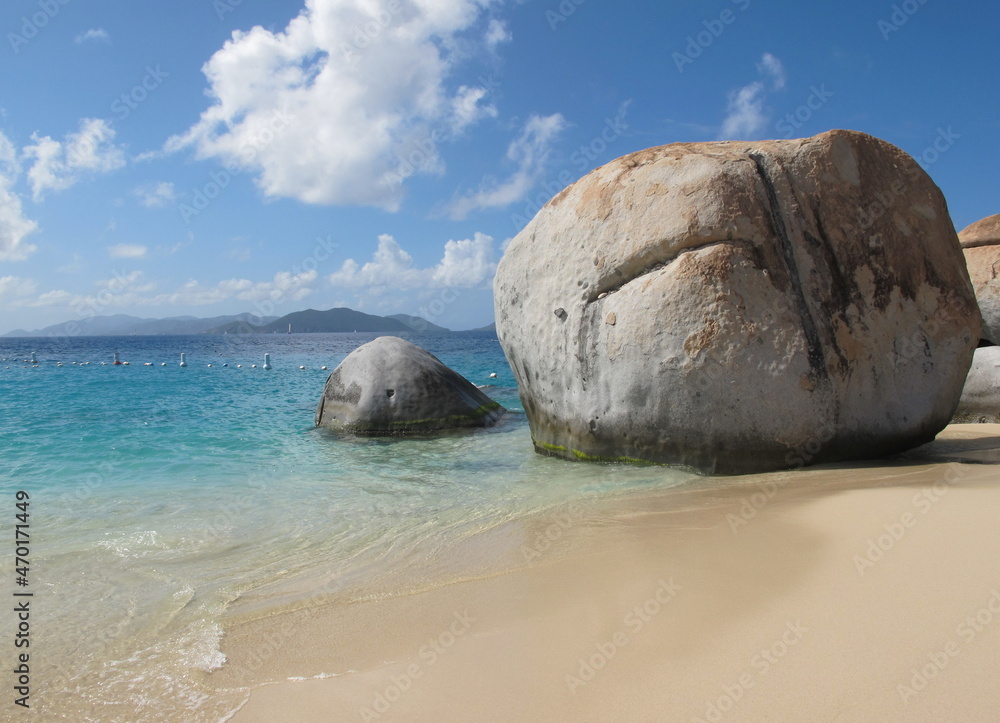 Fototapeta premium Huge spherical rock at the beach. Turquoise sea, brown sand, blue sky, clouds. Fissures or cracks in the rock. Virgin Gorda, British Virgin Islands, Caribbean, Devil's bay.