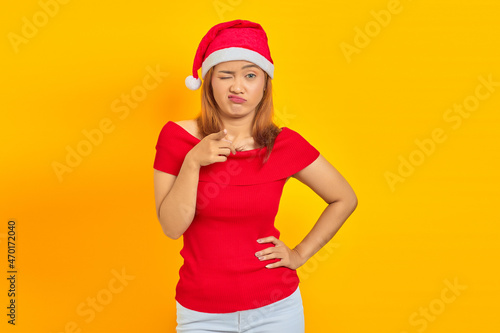 Portrait of sad young Asian woman with hands on waist and wearing Christmas hat on yellow background © Bangun Stock Photo
