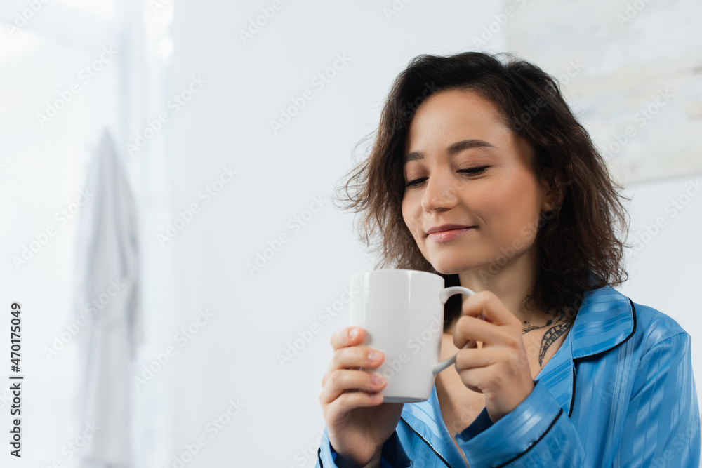 pleased woman in blue pajamas holding cup of coffee in bedroom. pleased woman in blue pajamas holding cup of coffee in bedroom.