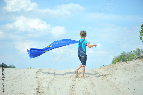 The child runs with the European flag against the background of a blue sky.