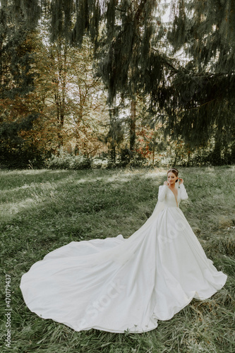 Wonderful bride in a white dress stands on a background of a large tree. 