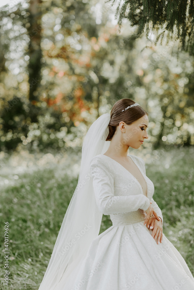 Portrait photo. The bride in a beautiful white dress stands with her back and poses for the camera