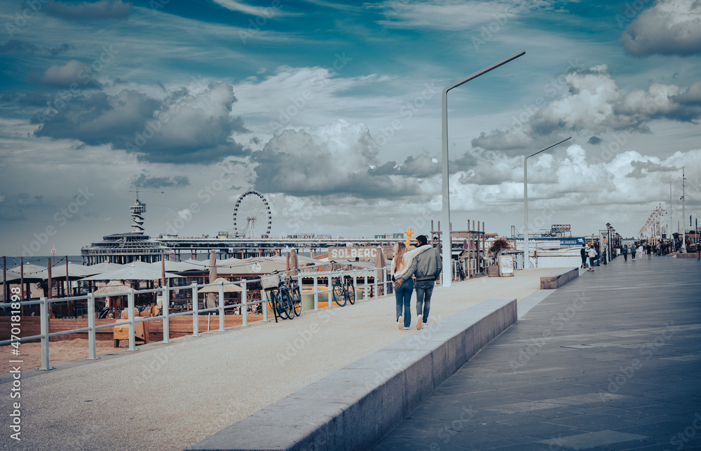 Zakochana para spacerująca promenadą nad morzem w Scheveningen, Holandia. - obrazy, fototapety, plakaty 