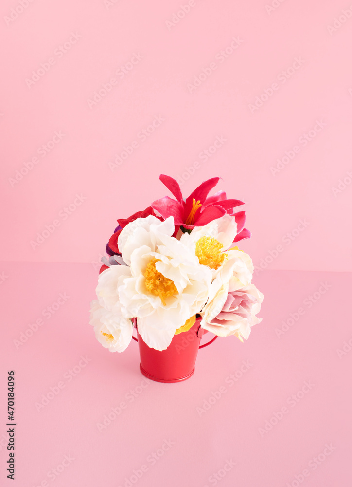 Colorful, exotic flowers in red metal bucket against pastel pink background. Creative layout, decorative floral element, gardening idea, growth, care, passion.