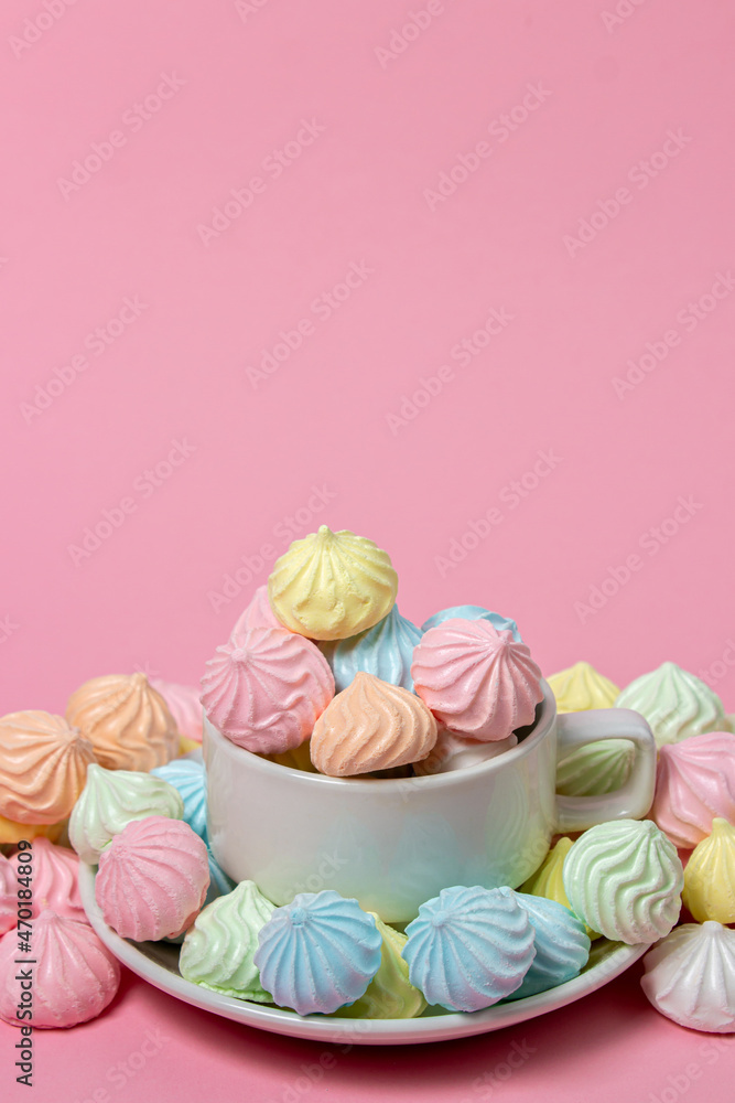 Multicolored meringues on a pink background. A teacup overflowing with colored meringues. Multicolored meringues on a pink background. A teacup overflowing with colored meringues.