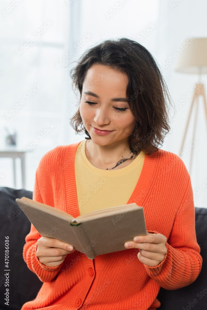 pleased and tattooed woman reading book at home. pleased and tattooed woman reading book at home.