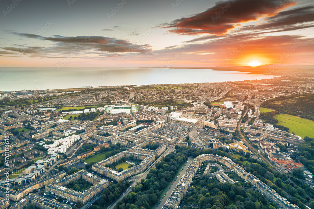 Sunrise over the city lights of Edinburgh. Aerial view of Edinburgh as the sun rises over the city. Early morning mist creeps along the shoreline of the North Sea like steam from a brewed coffee