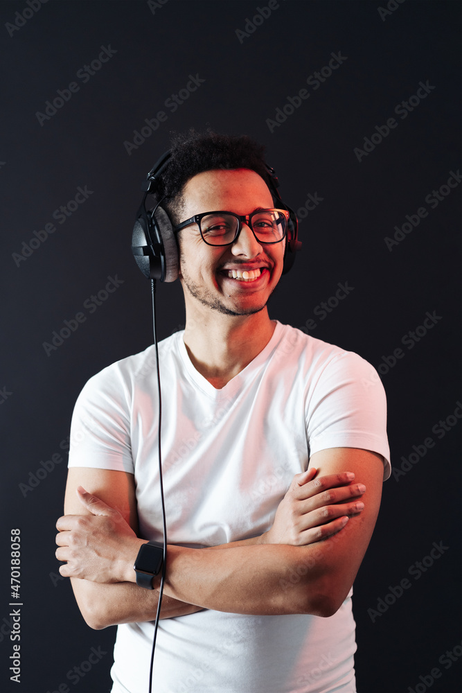 Young African American man wearing headphone, white t shirt and enjoy music over black Background. Red light reflecting on face. Emotions and face expressions Young African American man wearing headphone, white t shirt and enjoy music over black Background. Red light reflecting on face. Emotions and face expressions