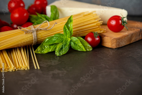 spaghetti on a dark background, cheese, tomatoes, and basil