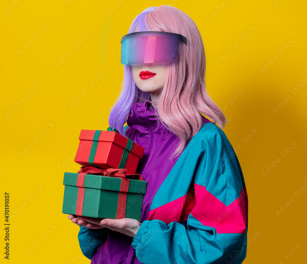 Style woman in VR glasses and 90s sport suit hold gift box on yellow background Style woman in VR glasses and 90s sport suit hold gift box on yellow background