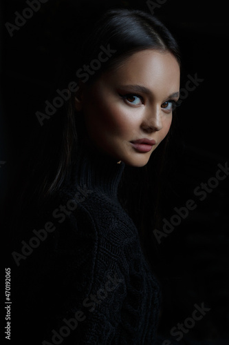 Stylish portrait of a beautiful brunette girl in a black sweater isolated on a black background.