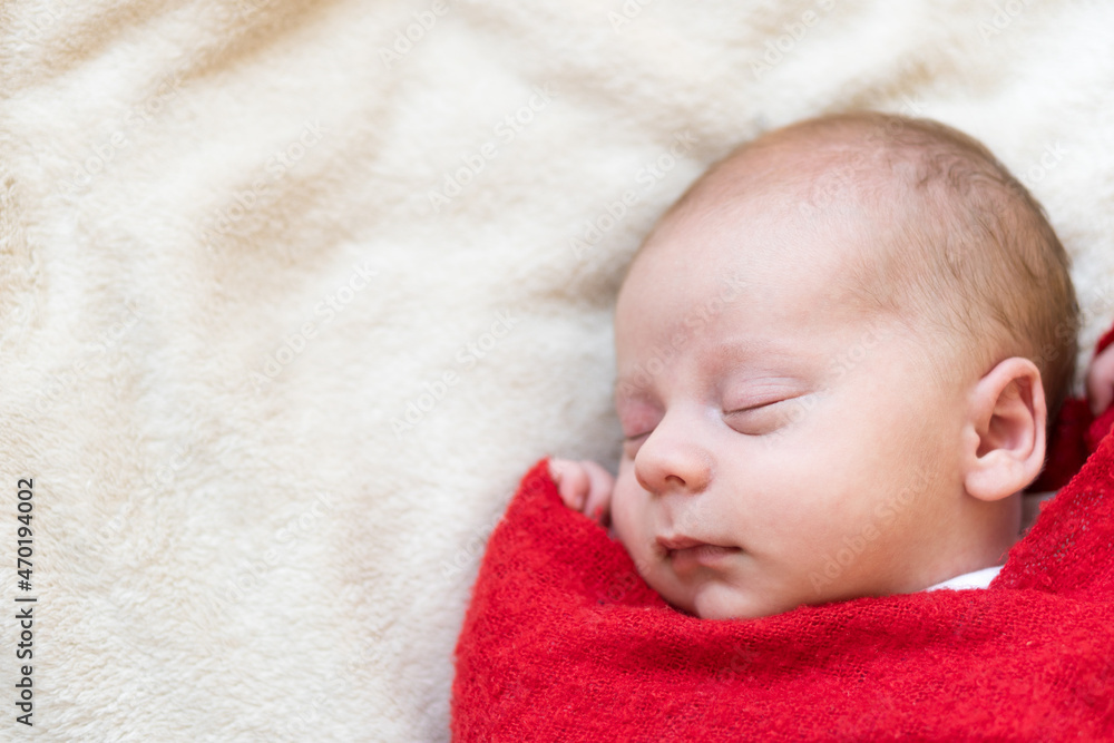 Top View Portrait First Days Of Life Newborn Cute Sleeping Baby In Santa Hat Wrapped In Red Diaper rug At White Garland Background. Merry Christmas, Happy New Year, Infant, Childhood, Winter Concept Top View Portrait First Days Of Life Newborn Cute Sleeping Baby In Santa Hat Wrapped In Red Diaper rug At White Garland Background. Merry Christmas, Happy New Year, Infant, Childhood, Winter Concept
