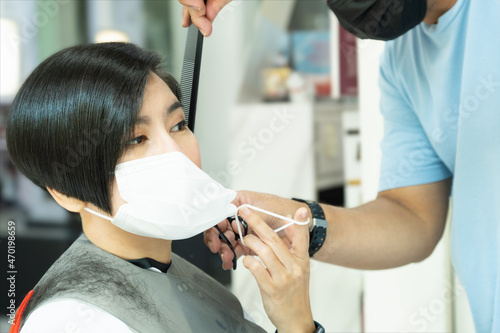 A beautiful asian woman getting haircut at a salons during Covid 19 pandemic, which face coverings is recommended for both hairdressers and client. Face mask, Restriction, Preventing, Safety, Rule.