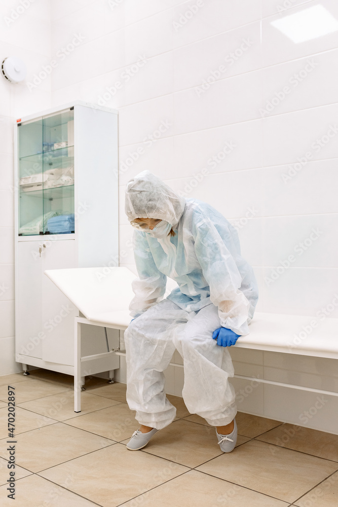 tired and sad female doctor in medical uniform, blue gloves, mask and glasses, sitting in a room for medical procedures tired and sad female doctor in medical uniform, blue gloves, mask and glasses, sitting in a room for medical procedures