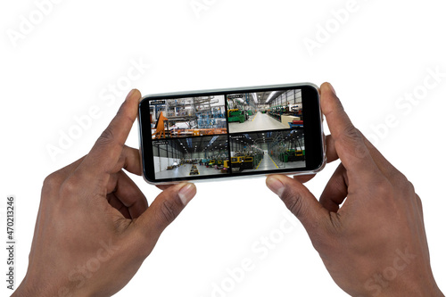 Hands of african american man holding smartphone, view of warehouse from security cameras on screen