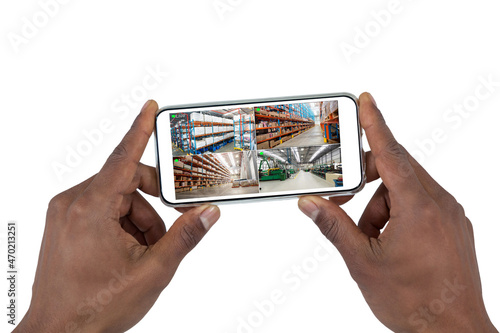 Hands of african american man holding smartphone, view of warehouse from security cameras on screen
