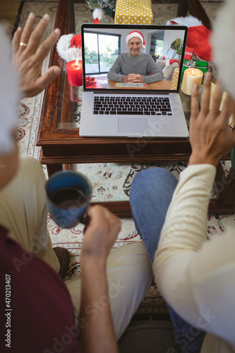 Two waving men making laptop christmas video call with smiling senior caucasian man in santa hat