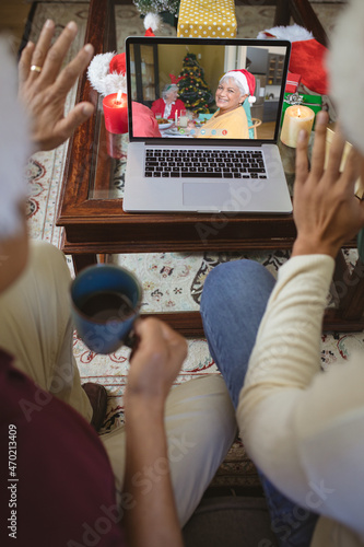 Two waving men making laptop christmas video call with smiling senior caucasian woman in santa hat