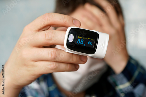 patient in a medical mask measures blood saturation with an electronic pulse oximeter on his finger.. pulse oximeter used to measure pulse rate and oxygen levels. low saturation of the blood. photo