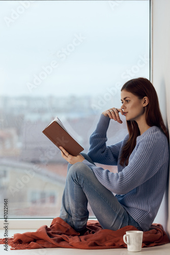 woman reading a book near the window with a cup of drink rest