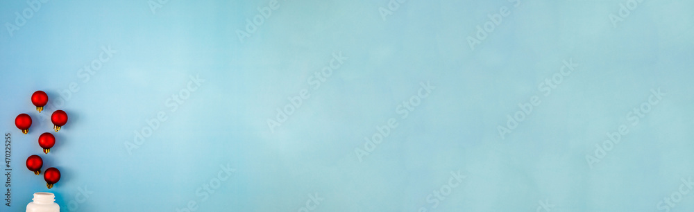 Naklejka premium Red Christmas balls like medicine pills blow out or ejection from bottle on blue background. Top view, flat lay, copyspace. Medical banner concept new year or Christmas. Winter holidays in pandemic.
