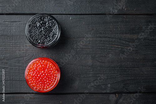 Glass jars with black and red caviar, on black wooden table background, top view flat lay with copy space for text