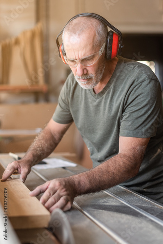Man with safety glasses cutting wood on sliding table saw