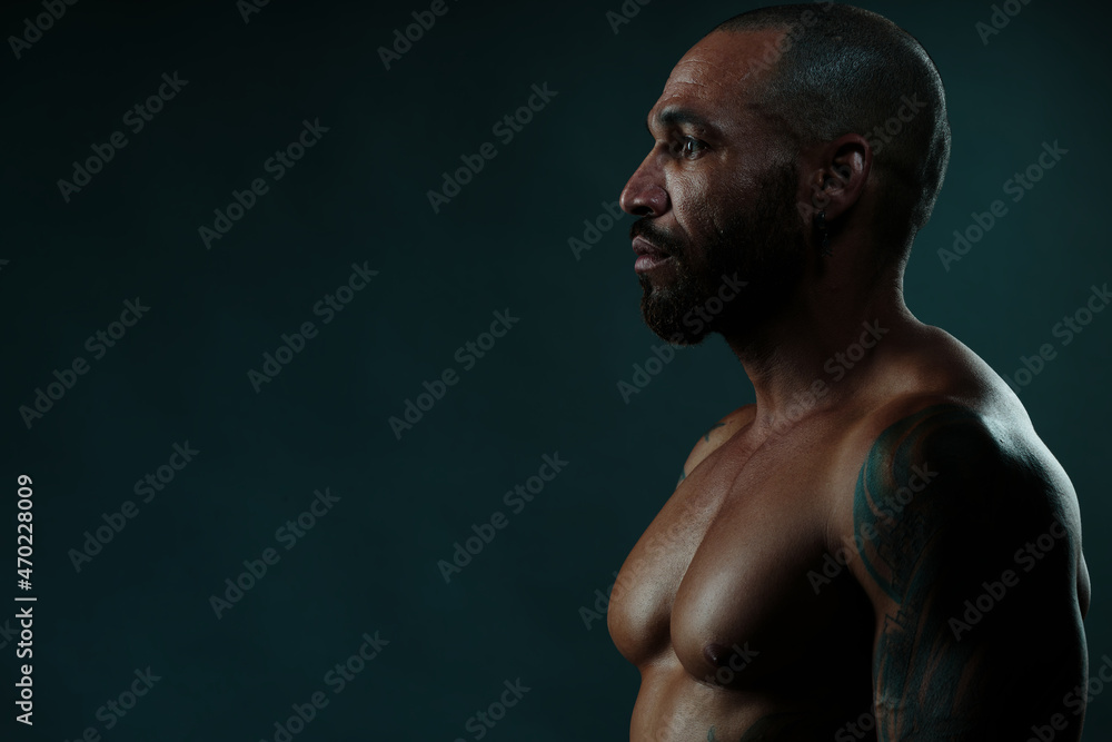 Studio portrait of African man in profile on dark background. Strong and muscular Cuban with naked torso. Side view. Studio portrait of African man in profile on dark background. Strong and muscular Cuban with naked torso. Side view.